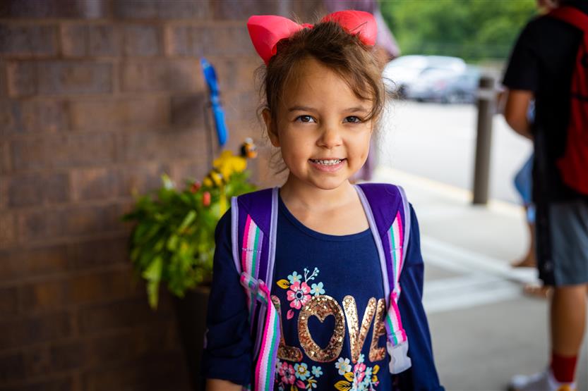 A girl with a red bow smiles